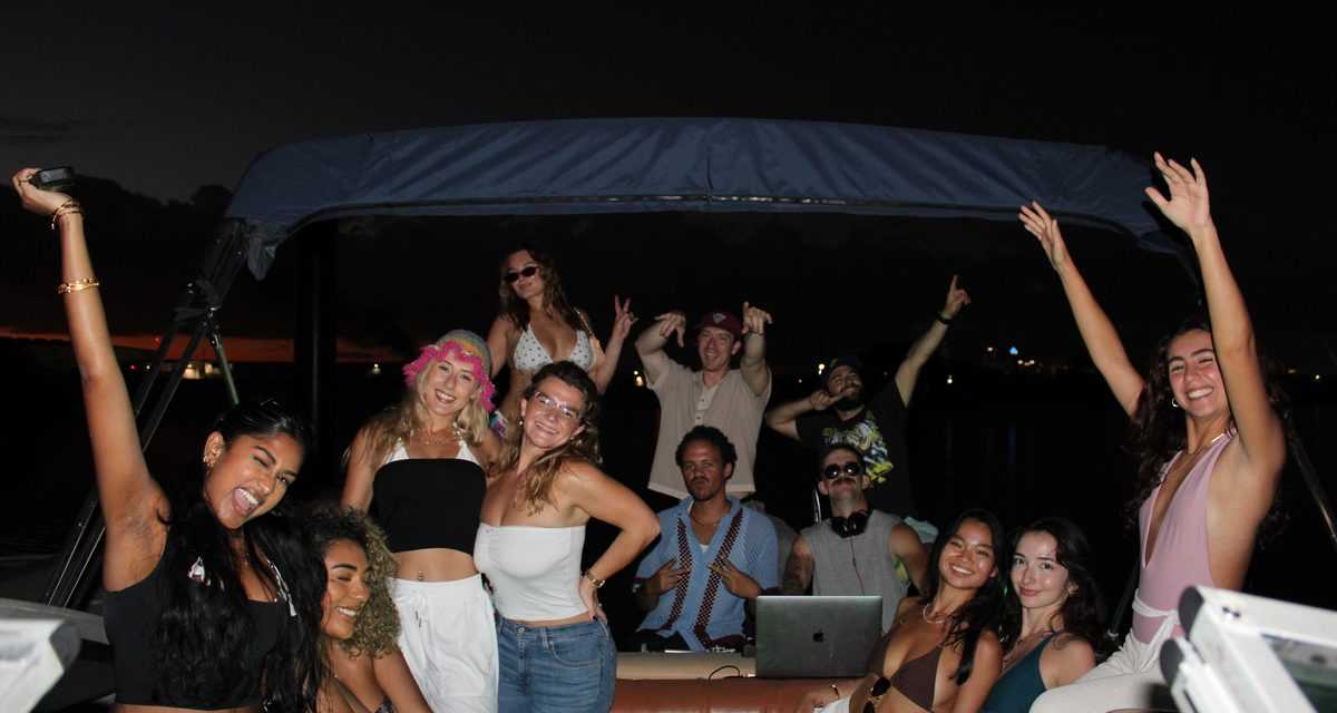 Guests with their arms up under the bimini lights on a Wave Rave night charter in Tampa.