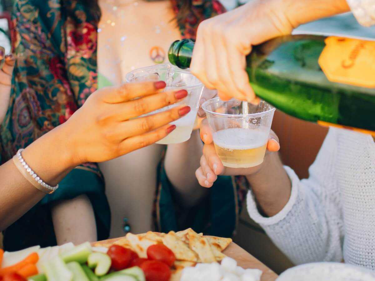 Champagne being poured into cups over a snack board on board.