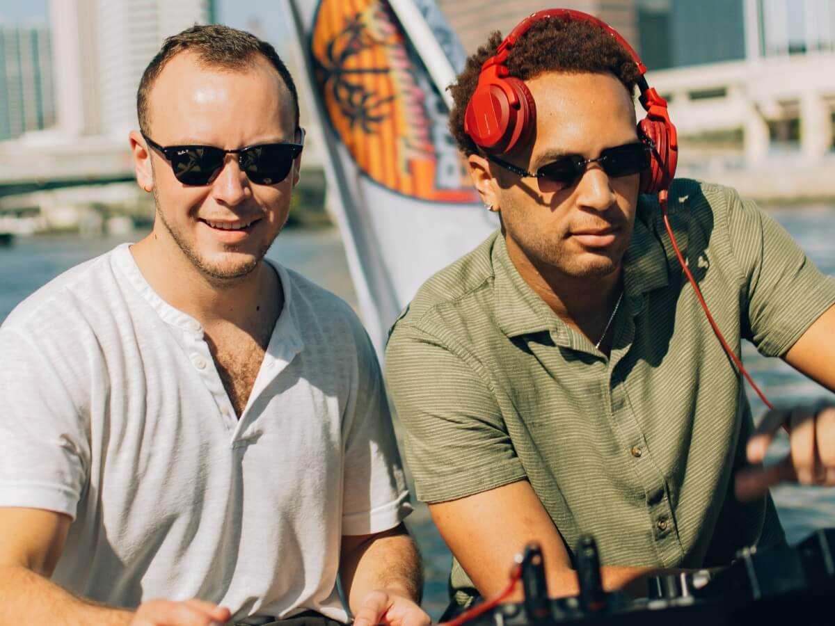 Two DJs mixing on board with the TBBA flag flying behind them.