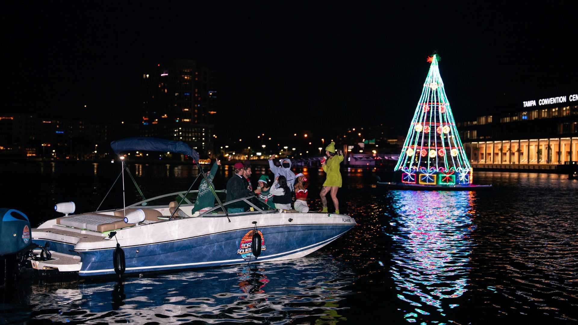 Friends enjoying a holiday boat cruise in downtown Tampa with lights reflecting on the water.